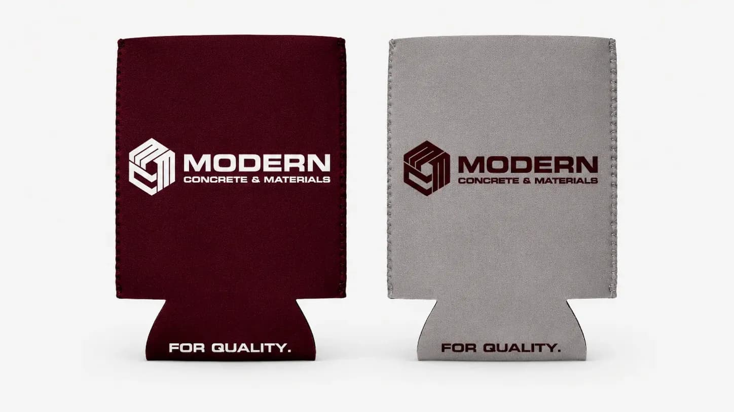 Two custom can coolers side by side, one maroon and one grey, printed with the Modern Concrete & Materials logo