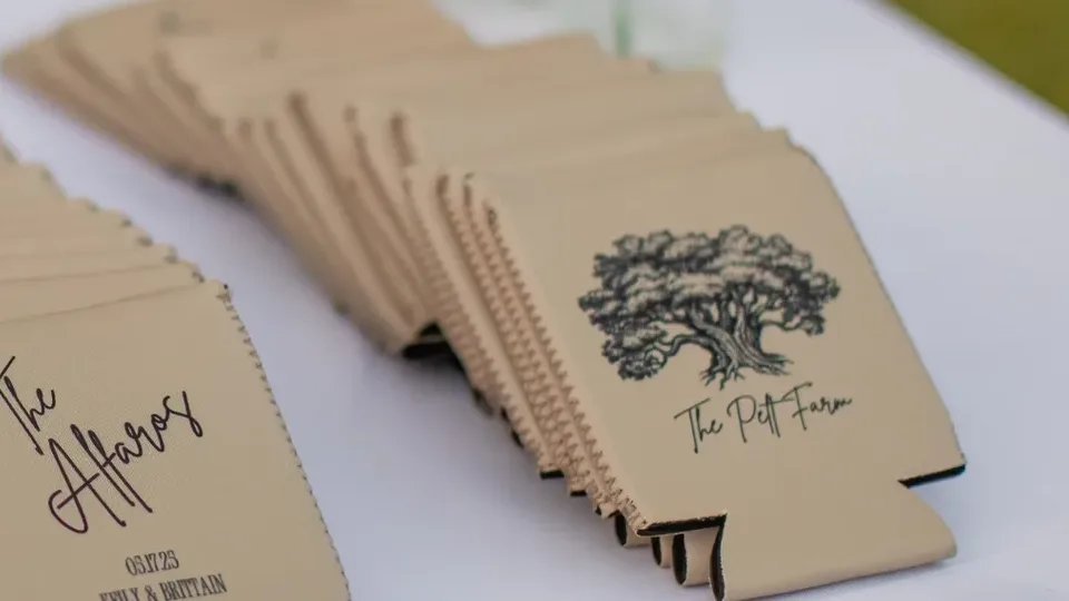 Stacks of tan wedding can coolers on a white table, one printed with an oak tree