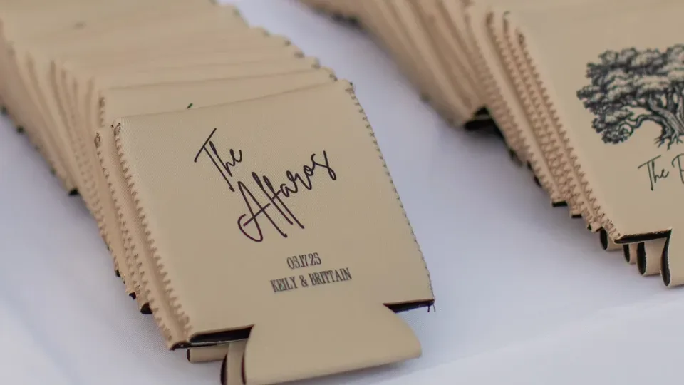 A stack of tan wedding can coolers printed with the couple's name and date on a white table
